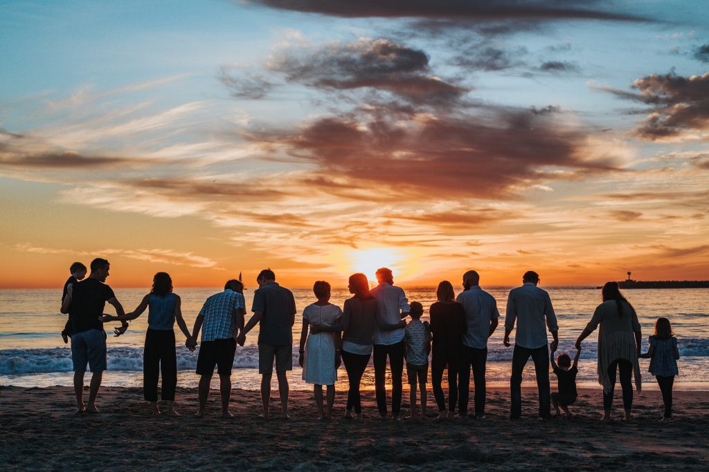 a family or a group of individuals facing the ocean at sunset and holding each other in unity